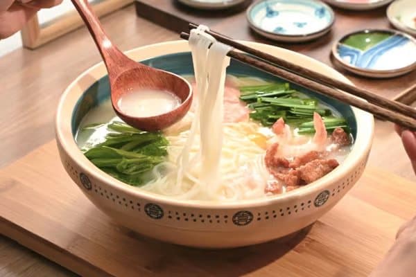 Crossing-the-Bridge Noodles — rice noodles being lifted from a steaming bowl
